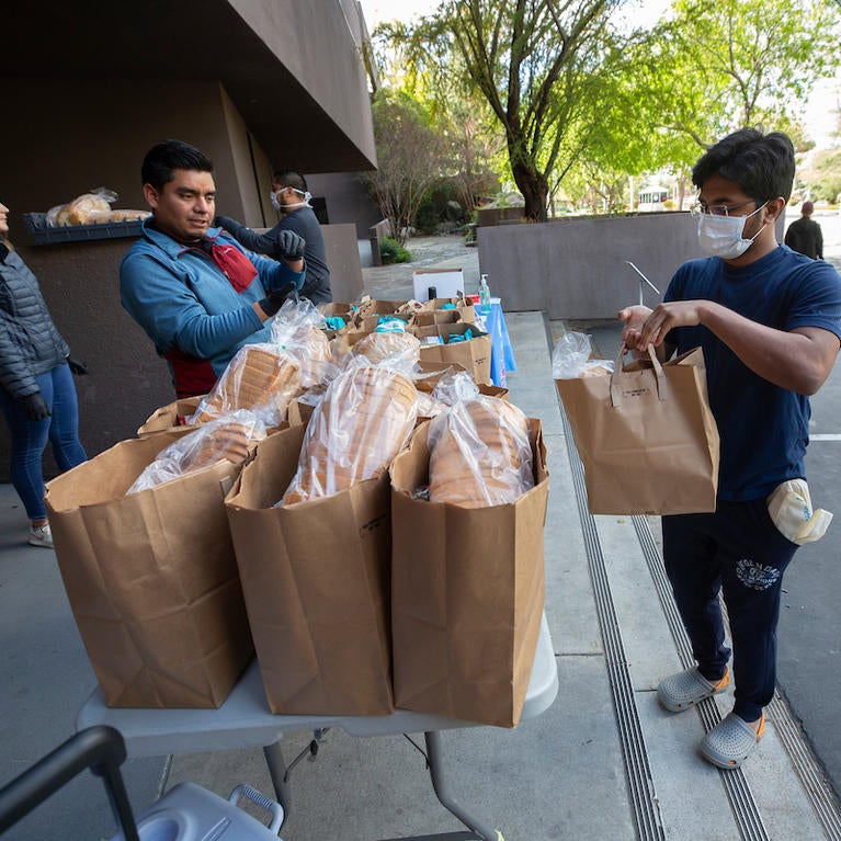 Grad student Saswat Nayak, 24, receives a bag of groceries from  R'Pantry coordinator Daniel Lopez Salas on March 26, 2020 at UC Riverside.  Staff with R'Pantry handed out bags of groceries to students after the campus was closed to help prevent the spread of the novel coronavirus. (UCR/Stan Lim)