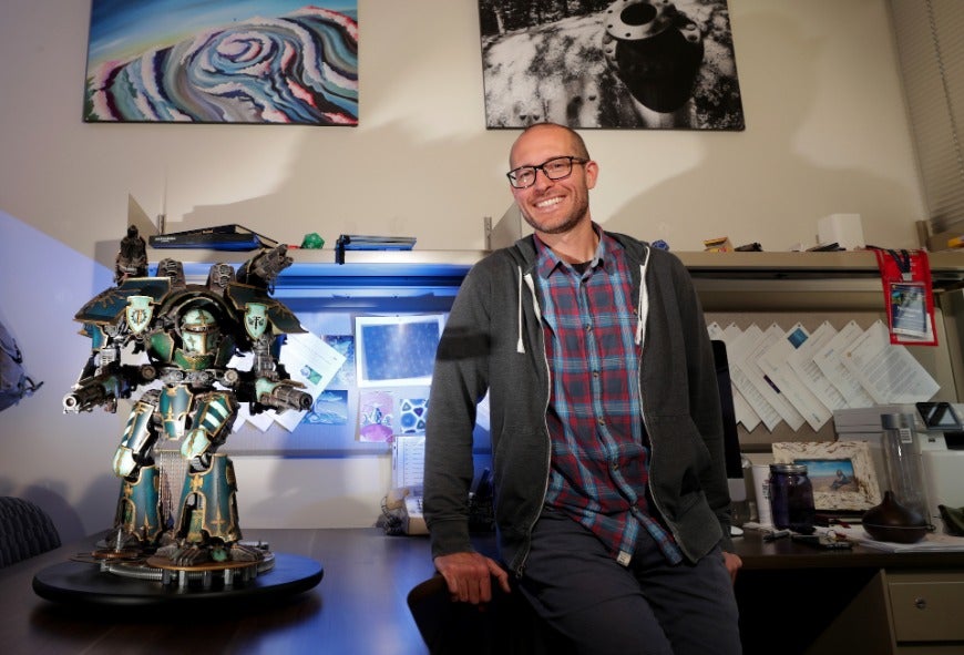 Nathan Gabor in his office with Warhammer titan sculpture on desk.