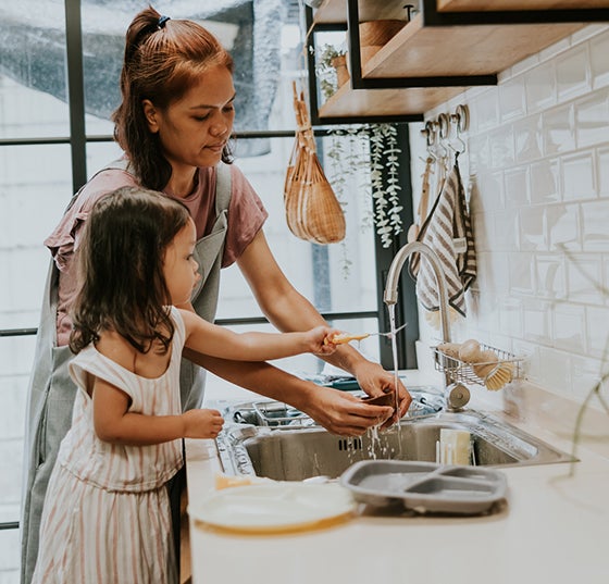 Mother and child daughter using a kitchen sink