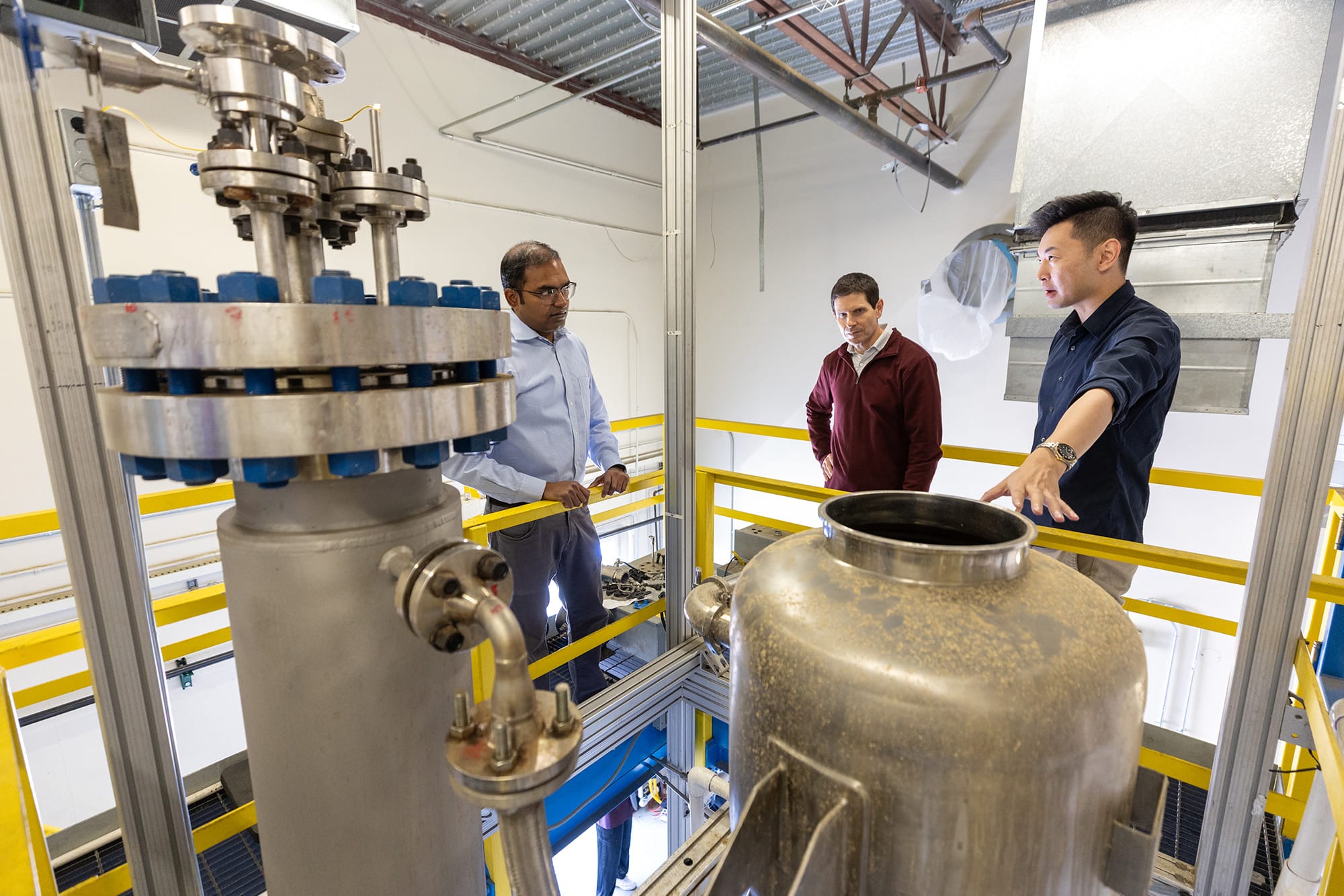 From left: Arun Raju, CE-CERT’s associate director of operations, and Don Collins, CE-CERT director, listen as Cai talks about his pilot-scale biomass processing unit.