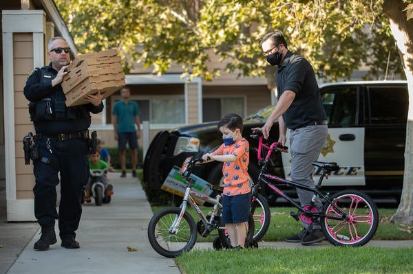 Police Officer Wade Stern, with the University of California Riverside Police Department, arrives with pizza as Jet Wilbur, 6, of Riverside, and his father, Robert Wilbur, a Master’s student of Educational Psychology in the School of Education, help push donated bikes from the UCPD to the Oban Family Housing at UC Riverside on Friday, September 17, 2021. (UCR/Stan Lim)
