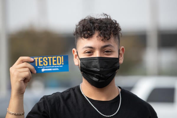 Student wearing mask holds Tested! sticker.