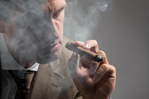 A well-dressed man smokes a cigar