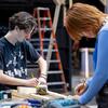 Students Tyler Yaish (left) and Aliche Zhang measure pieces of wood, preparing to cut them with a hand saw to add a trim to part of the set.