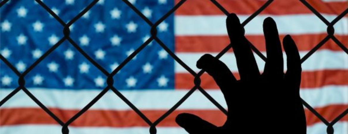 USA flag behind hand on chain link fence