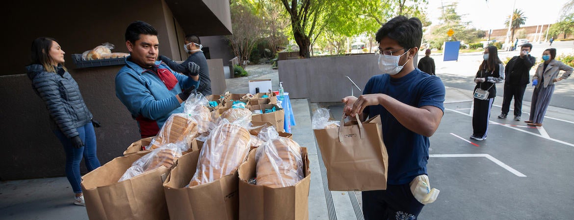 Grad student Saswat Nayak, 24, receives a bag of groceries from  R'Pantry coordinator Daniel Lopez Salas on March 26, 2020 at UC Riverside.  Staff with R'Pantry handed out bags of groceries to students after the campus was closed to help prevent the spread of the novel coronavirus. (UCR/Stan Lim)