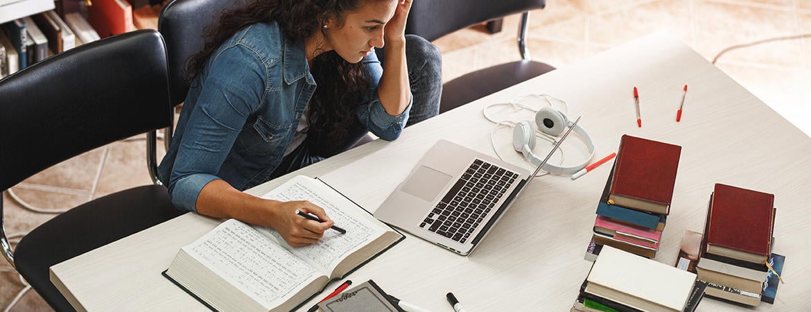 student studying at desk with laptop and textbooks