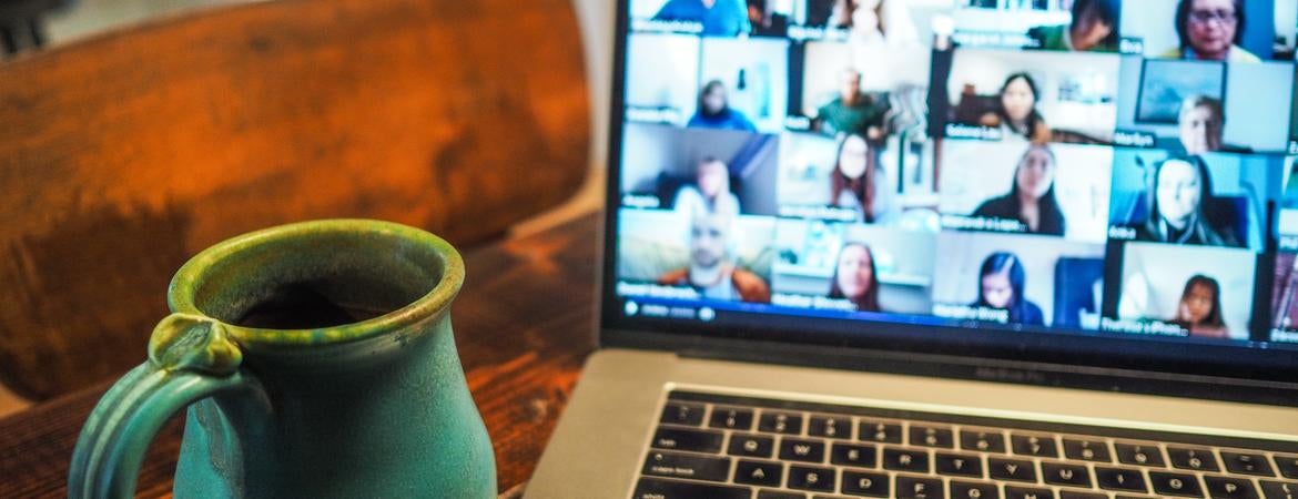 Laptop with video conference on a table with a green mug