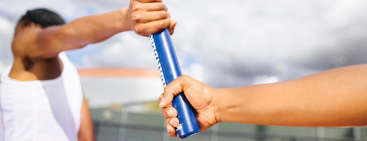 Two UCR runners pass the stick in a relay