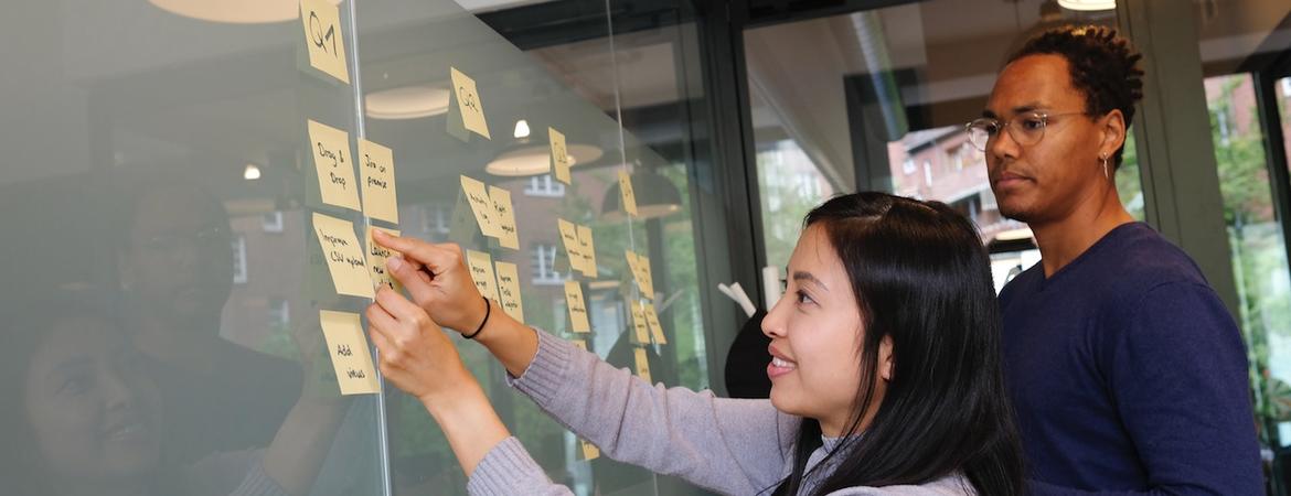 people putting sticky notes on a glass board