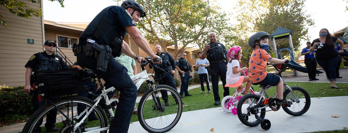 Police officer Paul Dombrowski, with the University of California Riverside Police Department, rides with Jet Wilbur, 6, front, and Claire Canale, 4, as they both ride donated bicycles at the Oban Family Housing at UC Riverside on Friday, September 17, 2021. Officer Dombrowski helped raise money from the department’s officers and staff to purchase the bikes for the children. (UCR/Stan Lim)