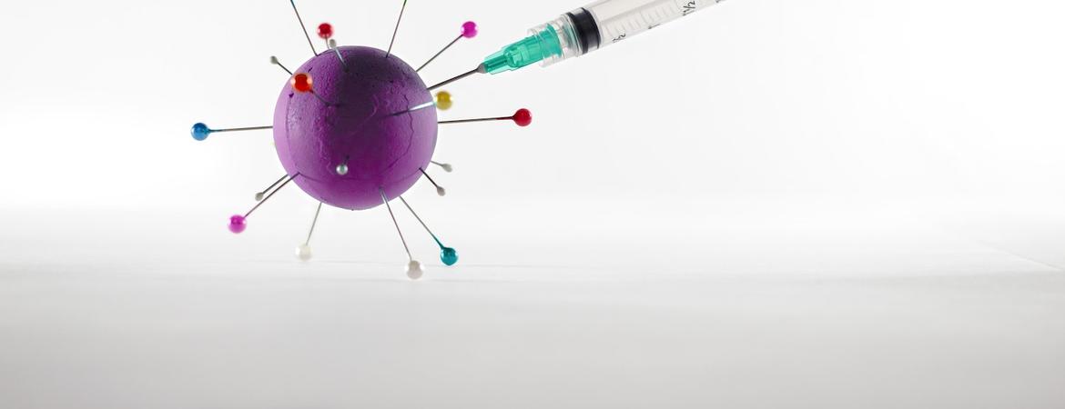 A syringe injecting a vaccine into a ball with pins that represents the covid-19 virus