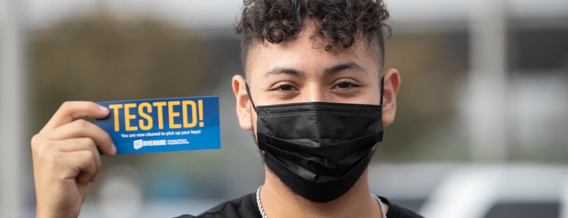 Student wearing mask holds Tested! sticker.