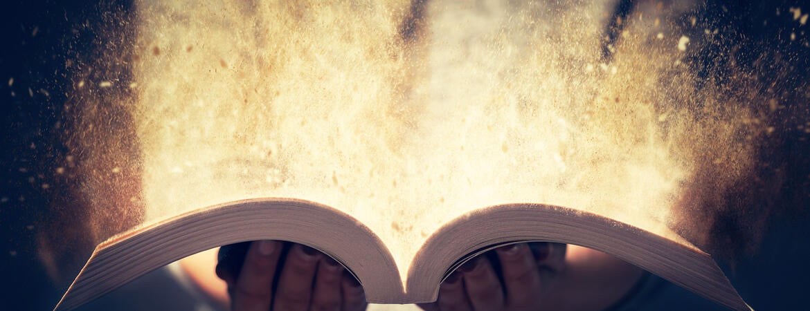 A person holds an open book and glowing light emerges from the pages
