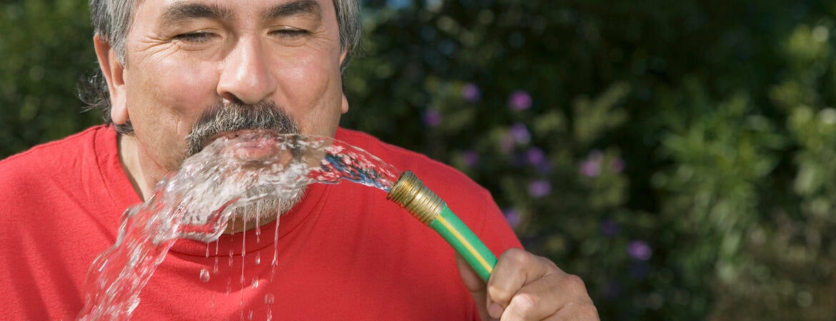 man drinking water from a hose