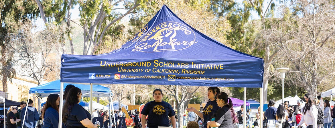 Underground Scholars students gather under a tent at an outdoor tabling event.