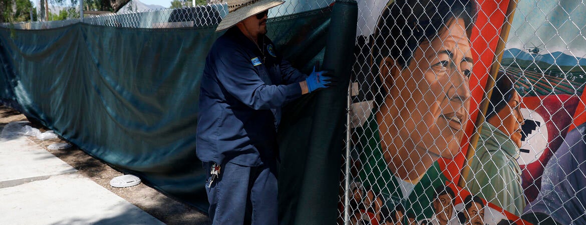 Workers cover up a fenced-off mural of César Chávez