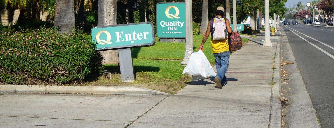 A man with bags walks past the Quality Inn in Riverside, Calif.