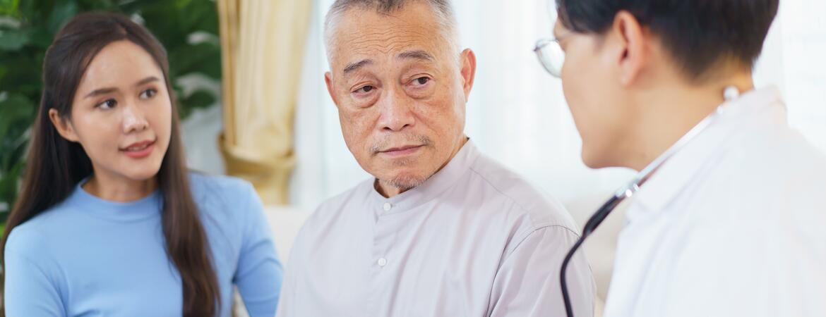Photo shows a doctor speaking with an elderly Asian man with his adult daughter present.