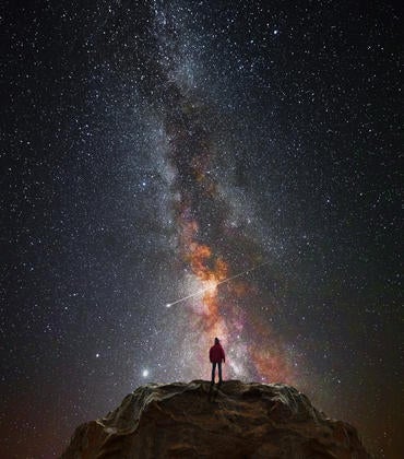 A man on a mountain looks at the stars.