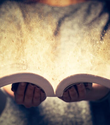 A person holds an open book and glowing light emerges from the pages