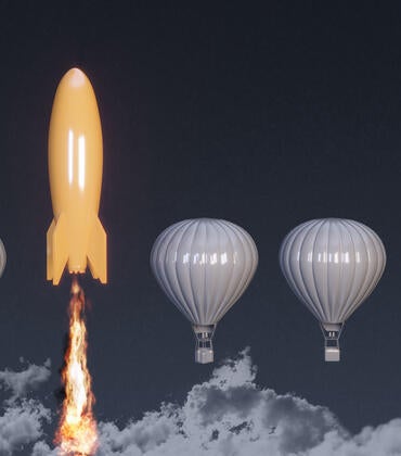 A yellow rocket takes off between gray hot air balloons