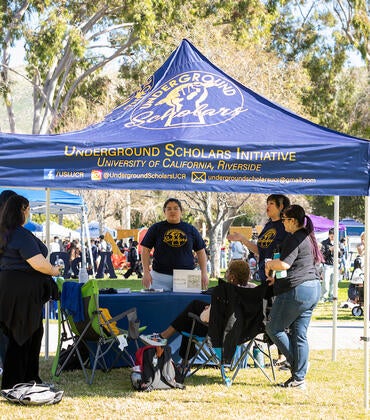 Underground Scholars students gather under a tent at an outdoor tabling event.