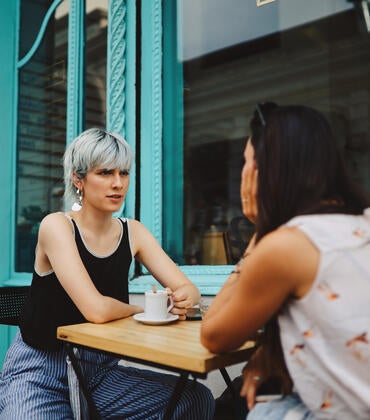 Two women talking at a table outside a cafe.