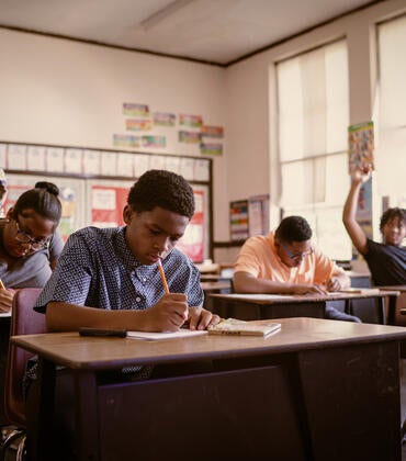 A teachers walks among students doing work at their desks.