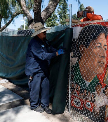 Workers cover up a fenced-off mural of César Chávez