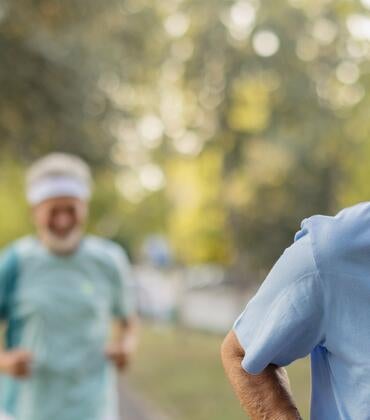 Two elderly men jog along a paved path.