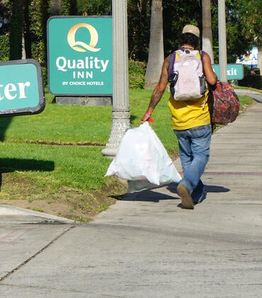 A man with bags walks past the Quality Inn in Riverside, Calif.