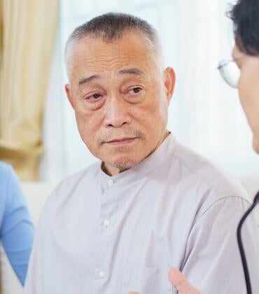 Photo shows a doctor speaking with an elderly Asian man with his adult daughter present.