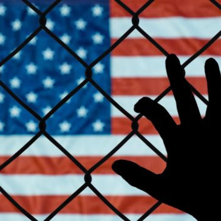 USA flag behind hand on chain link fence