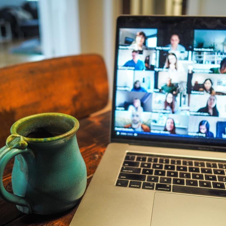 Laptop with video conference on a table with a green mug