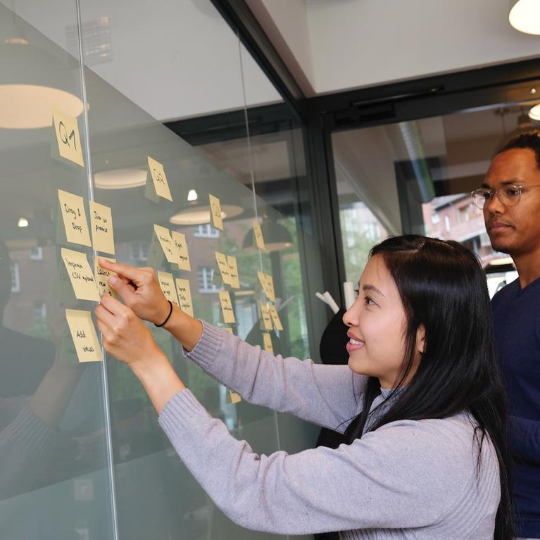 people putting sticky notes on a glass board