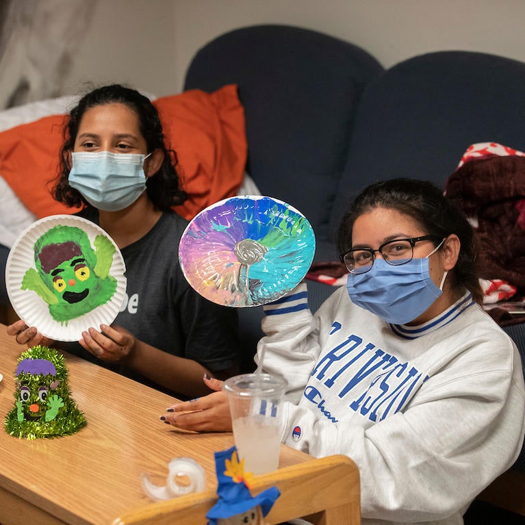 Marjorie Serrano, 18, left, and Miezue Primo, 18, show off their pain night creations as they interact with their resident advisor, Thomas Valenzuela, through Zoom at Pentland Hills Residence Hall on October 12, 2020. (UCR/Stan Lim)