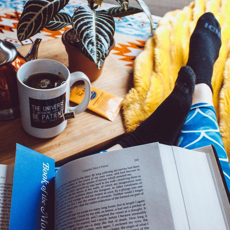 A person reading a book next to a cup of tea