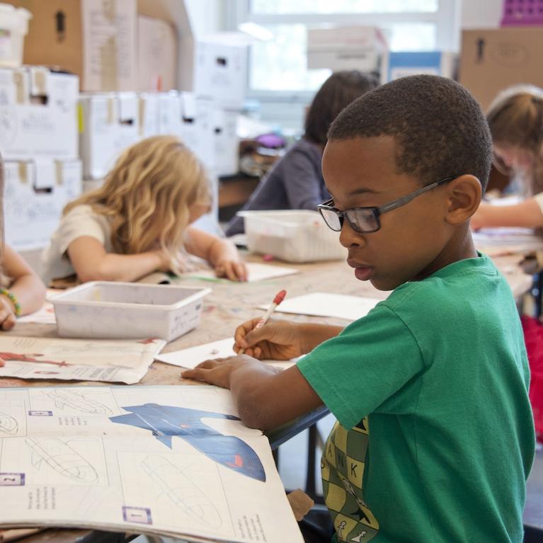 A child in a classroom absorbed in drawing an airplane.