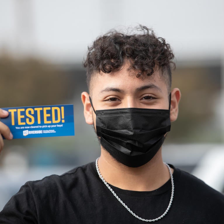 Student wearing mask holds Tested! sticker.