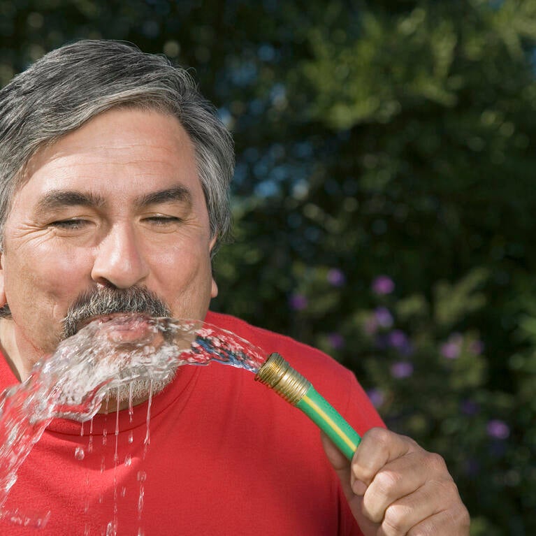 man drinking water from a hose