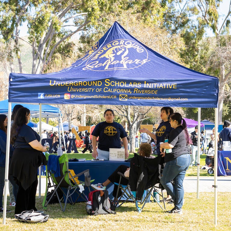 Underground Scholars students gather under a tent at an outdoor tabling event.