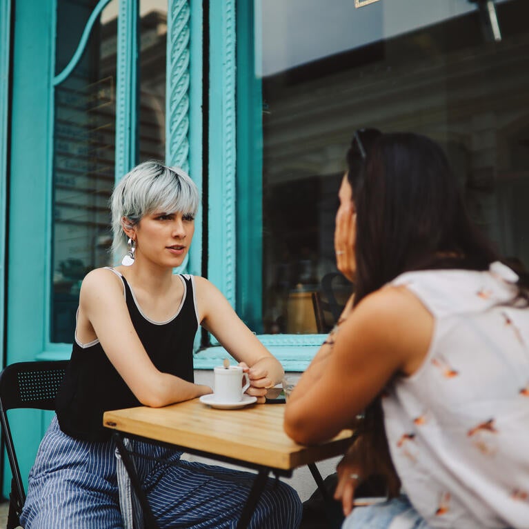 Two women talking at a table outside a cafe.