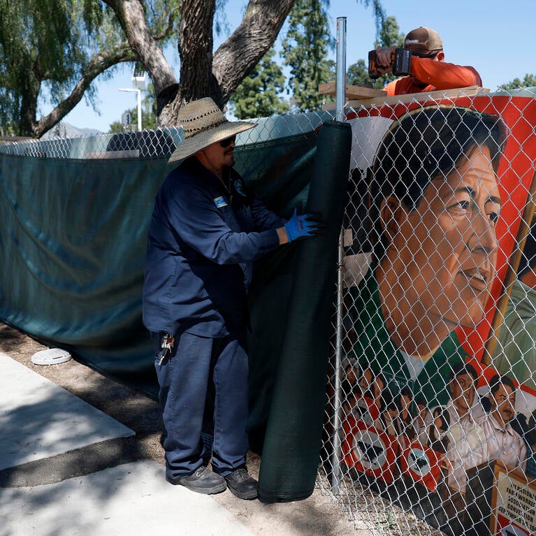 Workers cover up a fenced-off mural of César Chávez