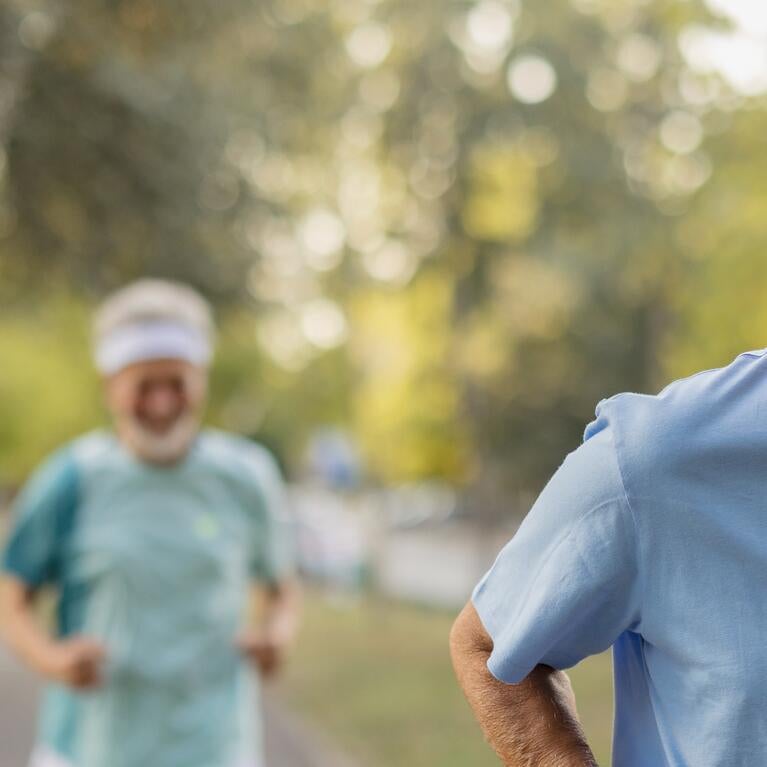 Two elderly men jog along a paved path.