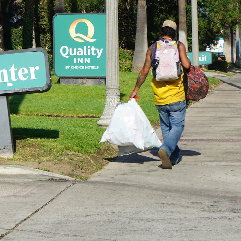 A man with bags walks past the Quality Inn in Riverside, Calif.