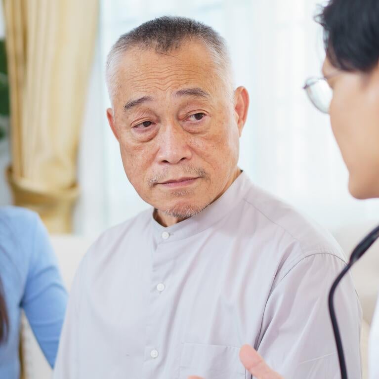Photo shows a doctor speaking with an elderly Asian man with his adult daughter present.