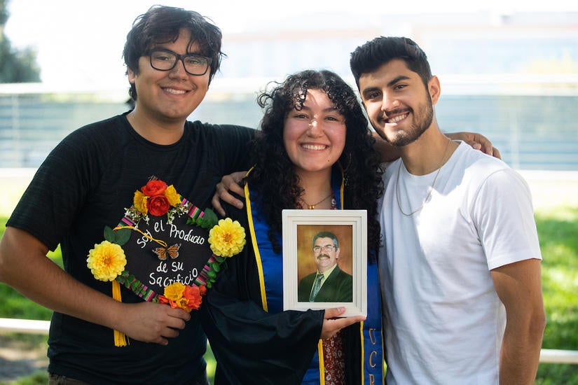 Itzel Pulido, 20, with her two older brothers, Javier (left) and Sergio Pulido, as Itzel holds a portrait of their late father. (UCR/Stan Lim) 