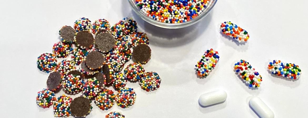 Chocolate drops covered with colorful candy nonpareils alongside pharmaceutical capsules also coated with the candy