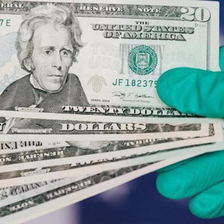 A gloved hand holds multiple $20 bills